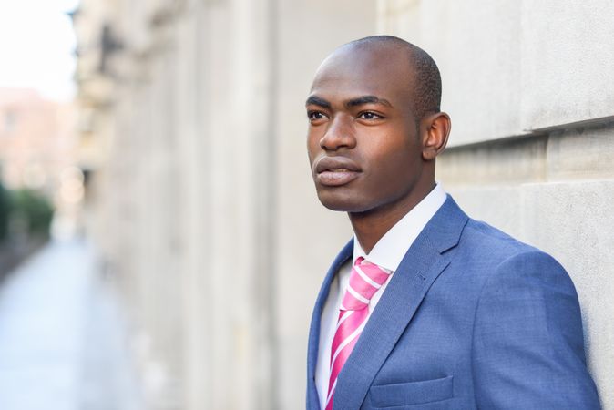 Serious male in business attire leaning on wall with copy space