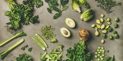 Arrangement of fresh green sliced garden vegetables on concrete surface, wide composition