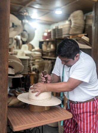 An adult Hispanic man is shaping a natural fiber hat
