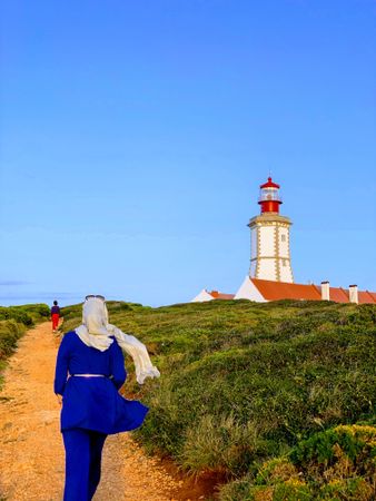 Woman in hijab walking towards lighthouse tower in Parque Natural da Arrabida in Setubal, Portugal 