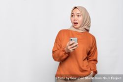 Surprised Muslim woman in headscarf and orange shirt with smart phone 41Lz85