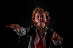 Child disguised as zombie with blood and glitter with arms raised walking