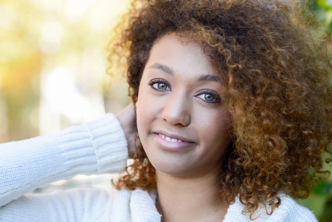 Portrait of woman with curly hair standing outside looking at camera and touching hair