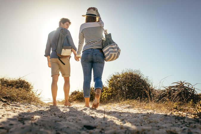 Man and woman enjoying holiday at a beach walking with their bags