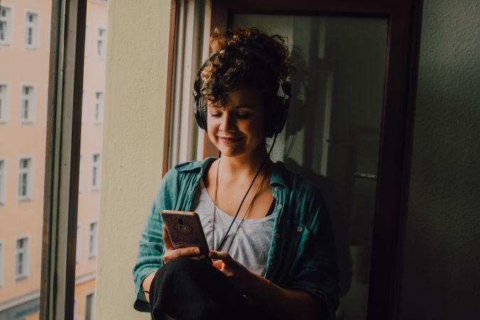 Cheerful woman in headphones using smartphone at home