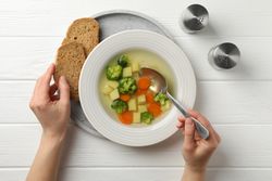 Looking down at person’s hands with spoon in vegetable soup