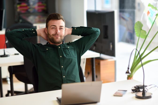Young man looking away from laptop computer in modern office