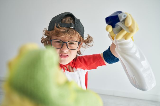 Curly boy in superhero clothes cleaning camera in studio
