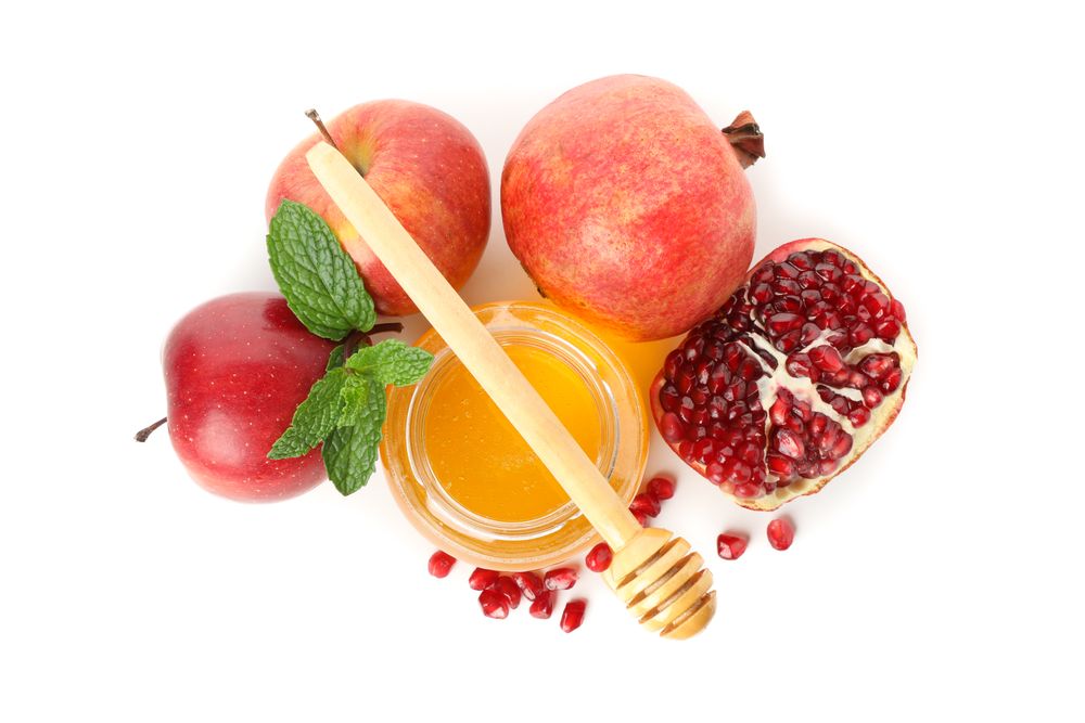 Top view of pot of honey with dipper, split pomegranate and apples