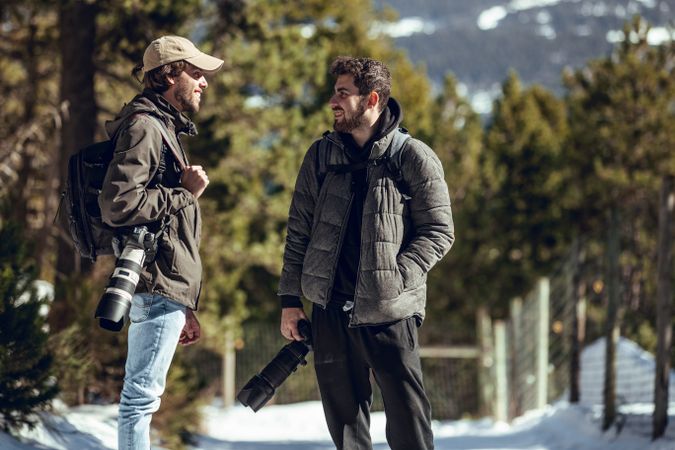 Positive men with cameras talking in winter forest