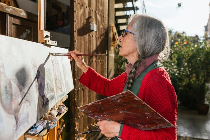 Older woman painting on canvas in garden