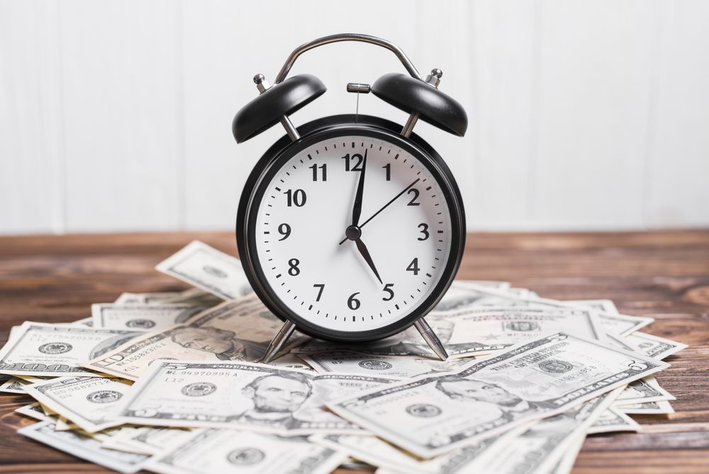 Alarm clock on spread currency notes over wooden textured background
