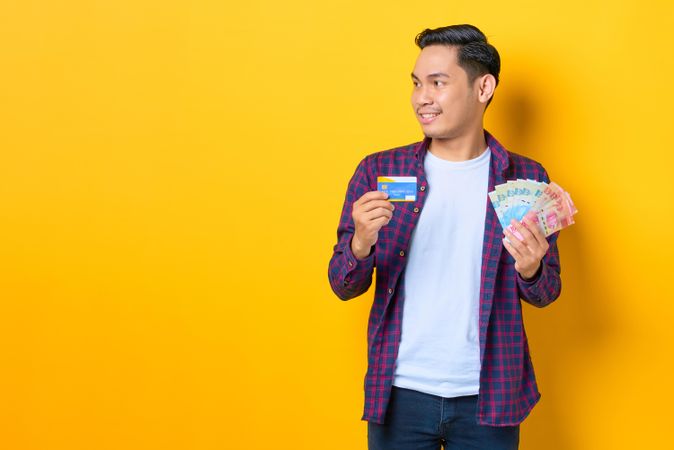 Man looking away while holding credit card and cash