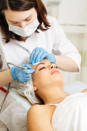 Woman having beauty treatment on face with machine on her forehead, vertical