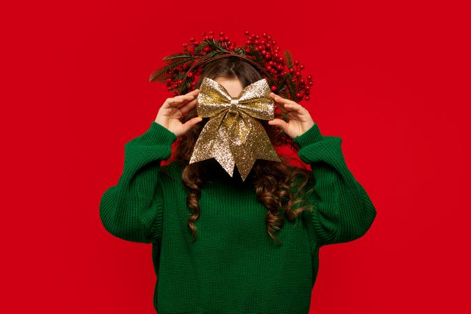 Young girl playfully hiding face behind large golden glittery bow.