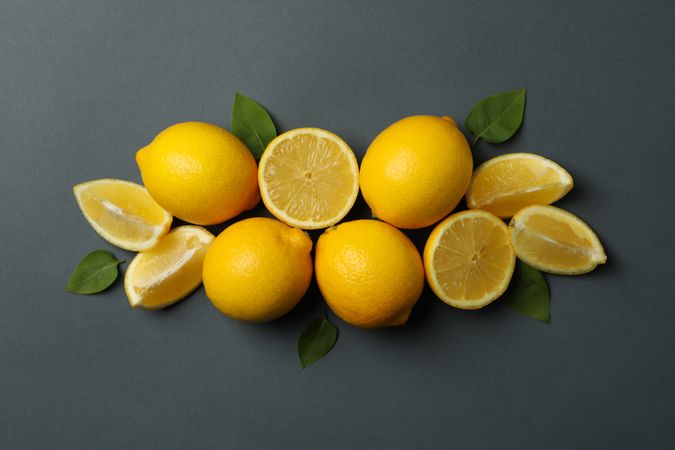Fresh lemons with leaves on dark background, top view. Ripe fruit