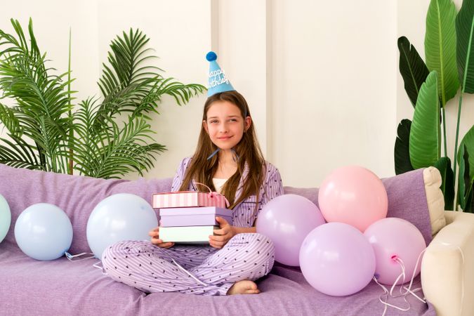 Girl holding gifts with balloons around on her birthday.