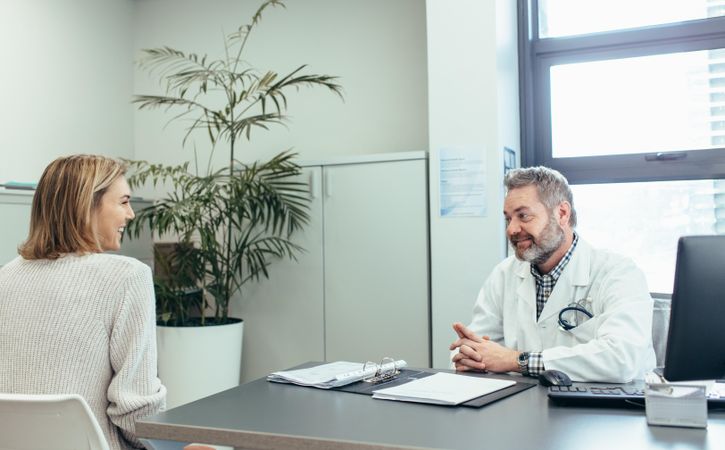 Happy medical doctor talking with woman sitting at office desk