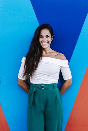 Elegant young woman leaning against a wall while looking camera and smiling