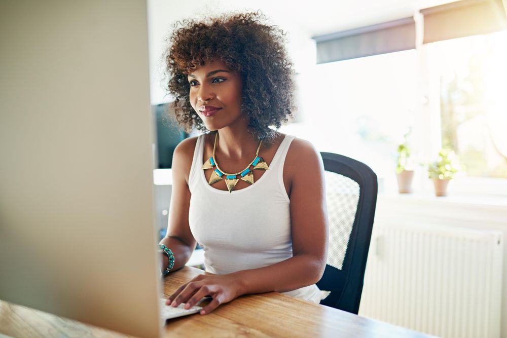 Female entrepreneur in bright office happily working on her computer in home office