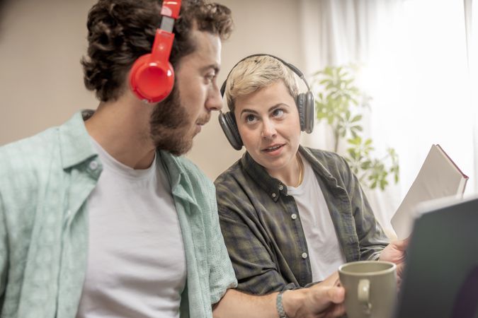 Man and woman with headphones collaborating on project in modern home office, e-learning or remote work.