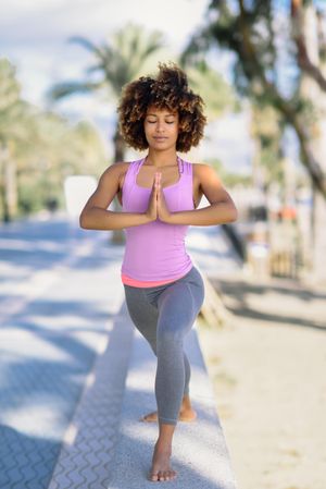 Front view of Black woman with afro hairstyle doing yoga warrior pose near beach