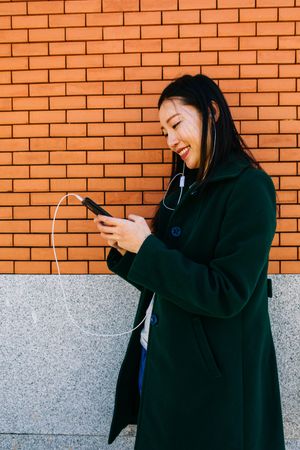 Asian female listening to music near brick wall