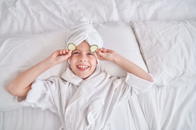 Boy taking off cucumber slices from eyes during spa procedures