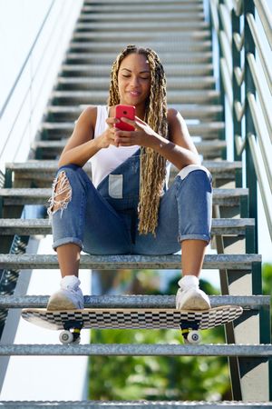 Smiling female skater checking phone on stairs