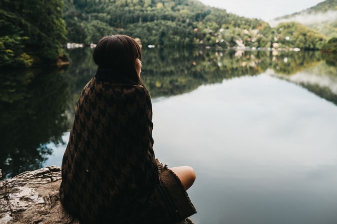 Woman sitting with blanket near lake and mountains