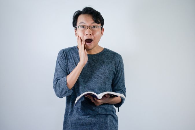 Asian young male reading book with surprised expression