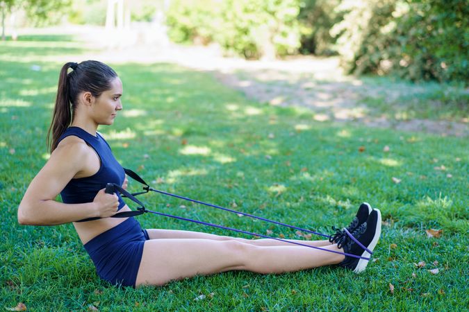 Woman exercises in park using resistance bands, showing dedication to fitness and stamina, visibly motivated