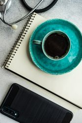 Coffee cup on teal plate, phone, stethoscope and notepad
