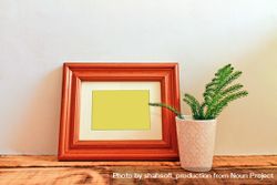 Wooden picture frame leaning against wall with branch in vase mockup 4j3ovb