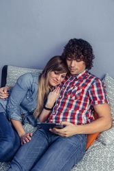 Couple cuddling while looking at electronic tablet in bed