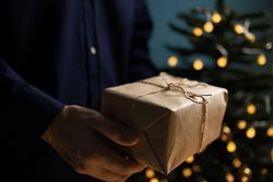 Man holding Christmas gift near tree