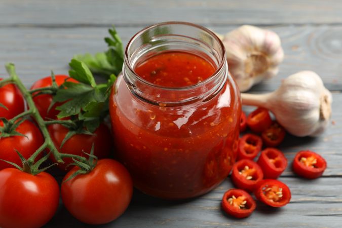 Jar with red chilli and tomato sauce, and spices on wooden table