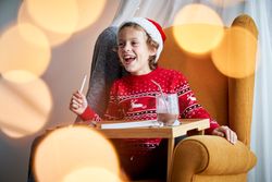 Happy boy in Santa hat writing letter on Christmas