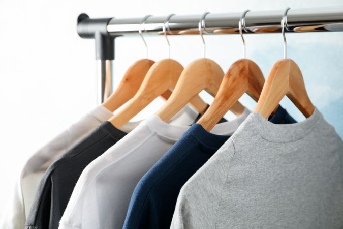 Rack with blank t-shirts on blue background, space for text