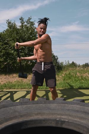 Muscular Black guy hammering tire in outdoor gym