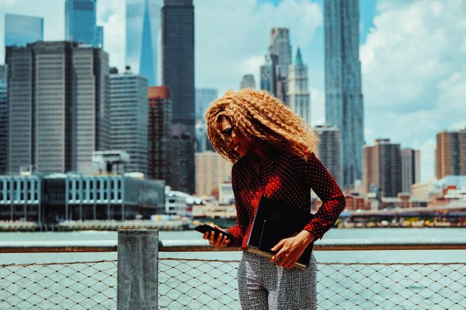 Happy professional Black female checking phone with Manhattan in the background