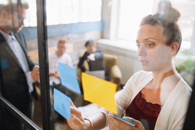 Woman looking at adhesive notes on window in meeting