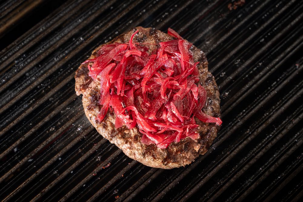 Grilled burger patty topped with caramelized red onions on barbecue grill