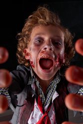 Vertical photo of a boy's face disguised as a zombie with blood and glitter with his hands in front of him and shouting