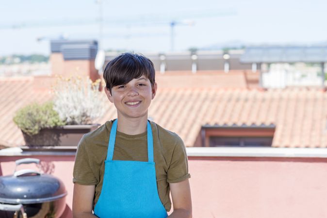 Portrait of smiling teenager standing on terrace wearing a gardener apron with copy space