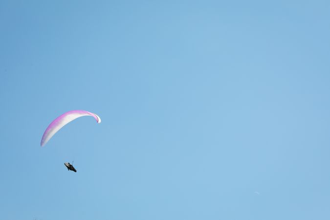 Skydiver with a pink parachute flies across the blue sky