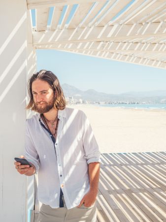 Relaxed man using smartphone in gazebo on beach