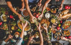 Group of people at wooden table with meze feast, serving toasting with white aperatif