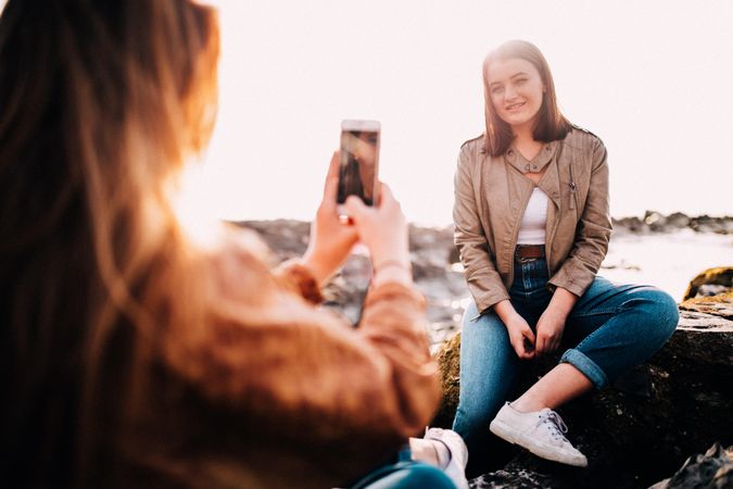 A young woman sitting outside has her photo taken by a friend