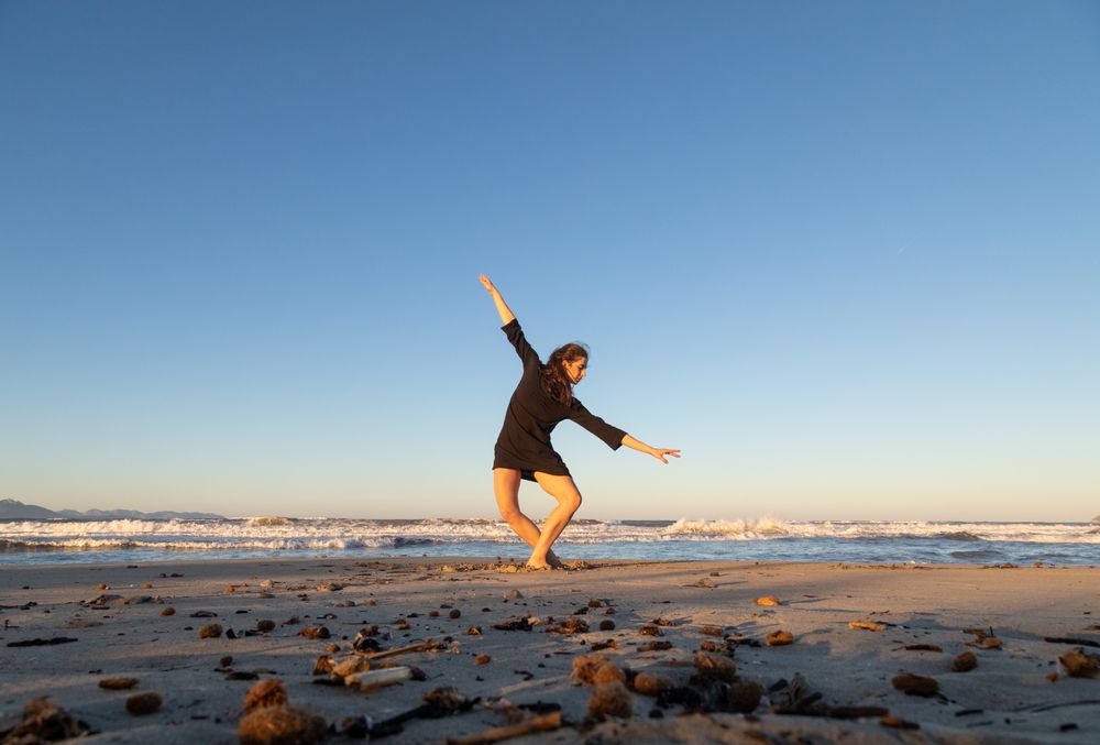 Young woman dancing and posing near water on shore